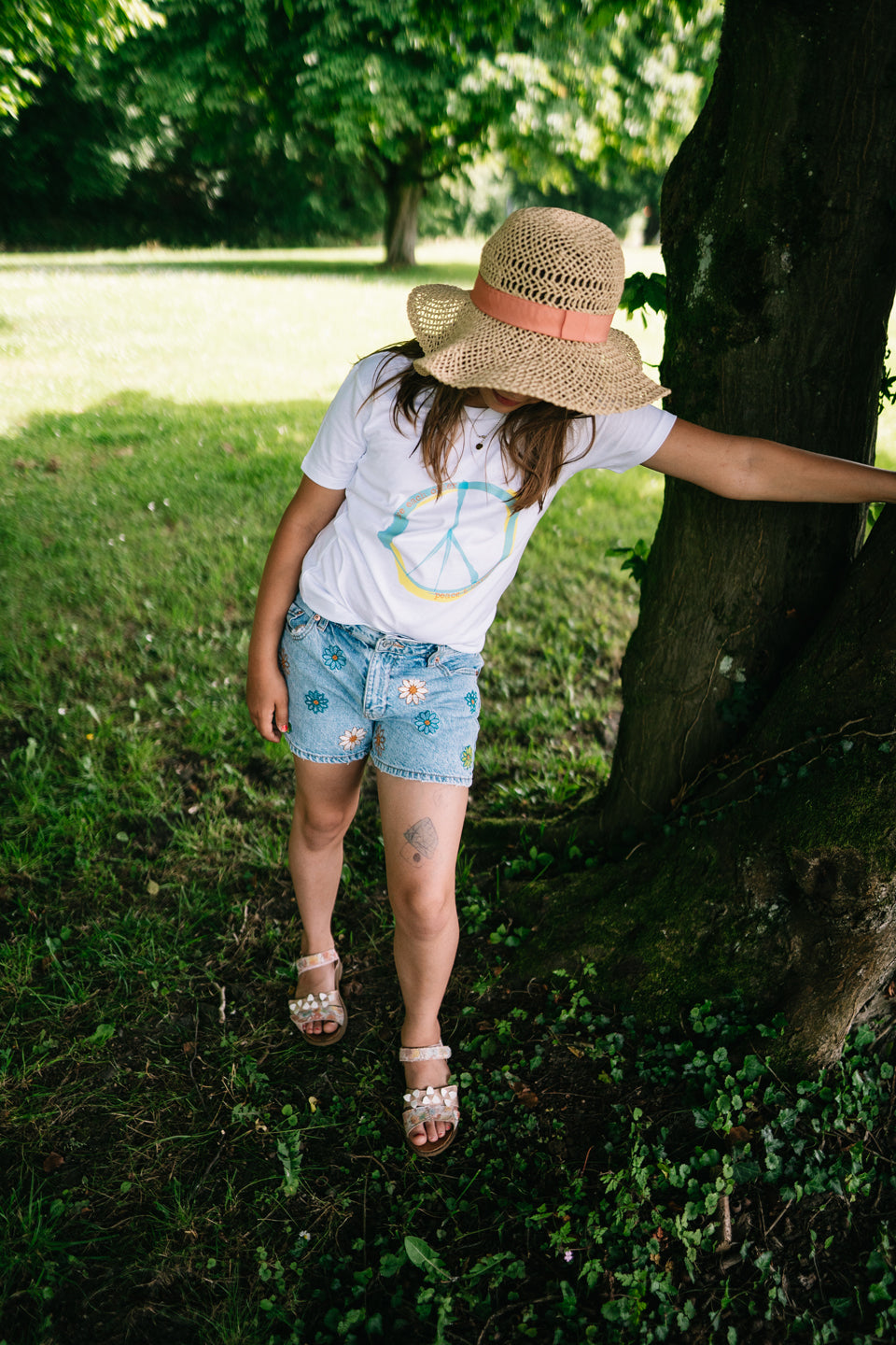 Ein Mädchen trägt einen sommerlichen Casual-Look und zeigt, wie man das weiße T-Shirt mit Peace-Print kombinieren kann.