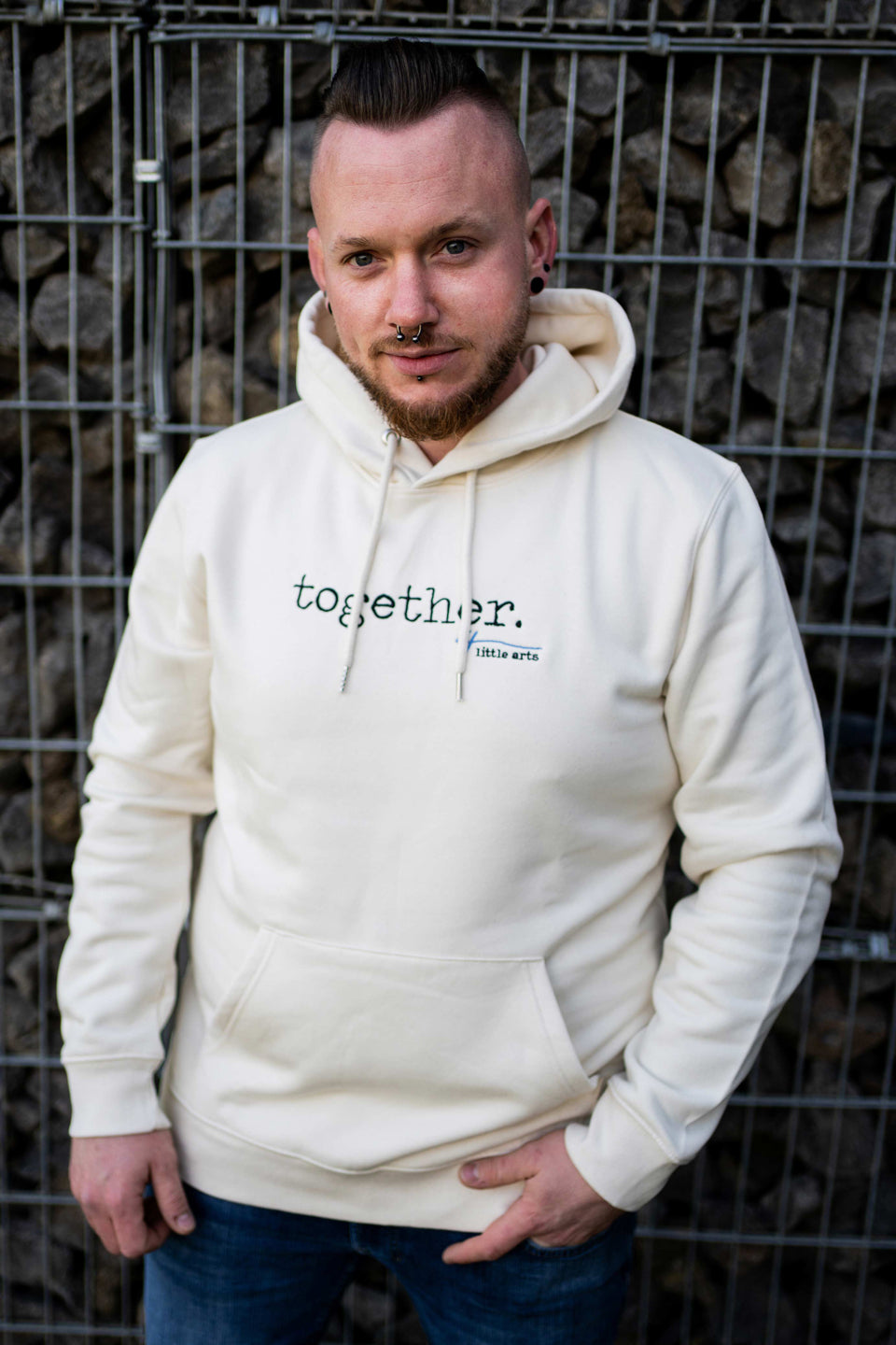 Ein Männermodel trägt den cremefarbenen Unisex-Hoodie mit dem gestickten Schriftzug 'together' auf der Brust.