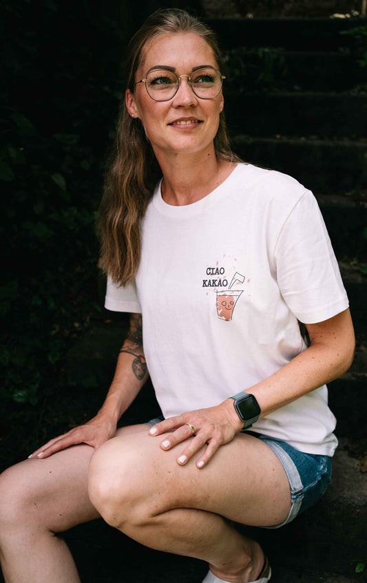 Ein Model trägt das Unisex-T-Shirt Ciao Kakao. Es ist Cremefarben aus recycelten Materialien und hat einen kleinen Druck auf der Brust.
